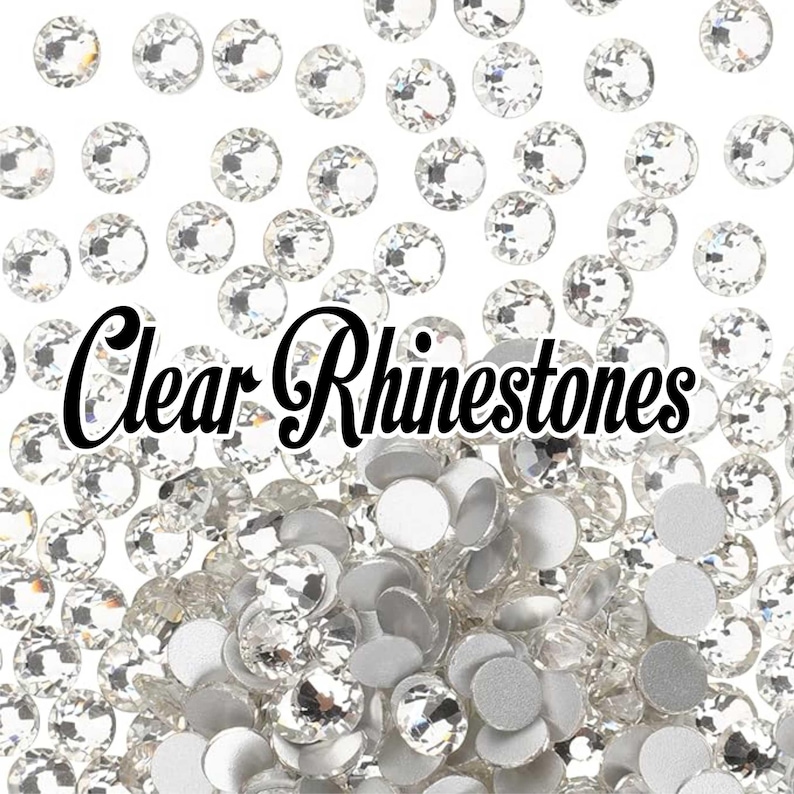 May include: A collection of clear rhinestones scattered on a white background. The image features a mix of faceted and flat-backed rhinestones, with the text "Clear Rhinestones" in a cursive font.