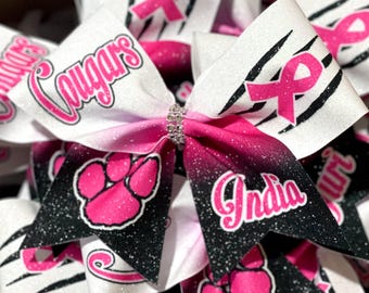 Peut inclure: Nœud de cheerleading avec un dégradé rose et noir. Le nœud présente le mot "Cougars" en script rose, une empreinte de patte rose et le nom "India". Le nœud a également un ruban rose et un centre en strass.