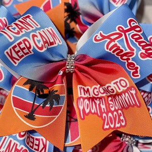 May include: A blue and orange hair bow with a palm tree design and the text "I'm going to Youth Summit 2023". The bow also has the text "Lady Amber" and "I can't keep calm" on it.