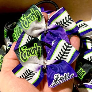 Puede incluir: Dos lazos para el pelo de color morado y blanco con ribetes verdes y negros. Los lazos tienen el texto "Every" y "Lady Raiders" impreso en ellos.