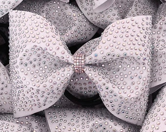 May include: A white bow with a silver rhinestone design. The bow is made of a soft, sparkly fabric and has a simple, elegant look.