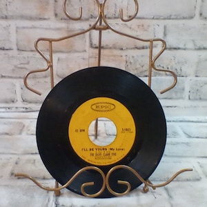 Puede incluir: Un disco de vinilo negro con una etiqueta amarilla en un soporte de metal dorado. La etiqueta dice "EPIC" y "I'LL BE YOURS (My Love) THE DAVE CLARK FIVE".