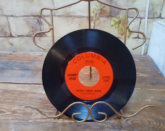 May include: A black vinyl record with a red label. The label says "Columbia" and "Johnny Cash" with the song title "Daddy Sang Bass".
