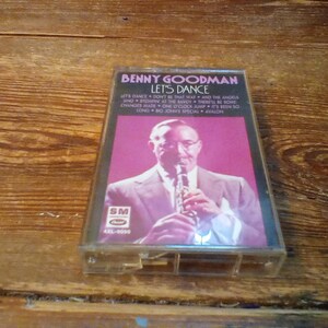 May include: A vintage cassette tape of Benny Goodman's "Let's Dance" album. The cover features a portrait of Goodman playing a clarinet against a pink background. The tracklist is visible. The cassette is in a clear plastic case.