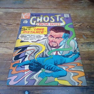 Può includere: Un fumetto vintage intitolato "The Many Ghosts of Doctor Graves". La copertina presenta un uomo in giacca e cravatta e un'altra figura in tuta blu, con il testo "Evil forces lurk in... Long Distance."
