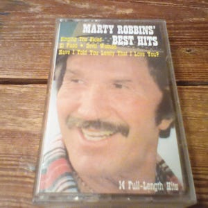 May include: A cassette tape featuring a portrait of Marty Robbins on the cover with the text Marty Robbins' Best Hits, Singing The Blues, El Paso, Devil Woman, Have I Told You Lately That I Love You?, and 14 Full-Length Hits printed in white and yellow.