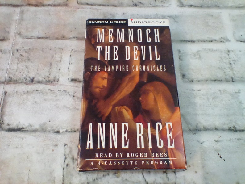 Puede incluir: Una caja de cassette roja y blanca con el t&iacute;tulo "Memnoch the Devil" de Anne Rice. La caja presenta una pintura de un hombre y una mujer, y el texto "The Vampire Chronicles".