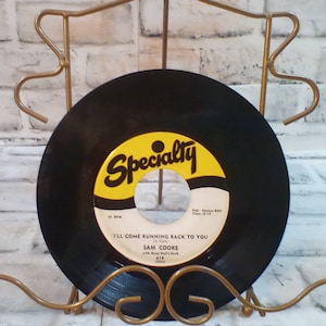 Peut inclure: Un disque vinyle noir avec une étiquette jaune. L'étiquette indique "Specialty" en lettres noires et "I'll Come Running Back To You" en lettres noires. Le disque est de Sam Cooke et est sur un support de disque en métal doré.