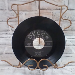 Peut inclure: Un disque vinyle noir avec une étiquette blanche. L'étiquette porte le texte "Decca" dans un cercle rouge avec une étoile. Le disque est intitulé "You Hit The Wrong Note" par "Billy Goat" avec "Bill Haley and His Comets". Le numéro du disque est 9-30314.