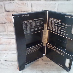 Puede incluir: Cuatro cajas de cassette negras con texto blanco. El texto en las cajas dice "Cassette 1", "Cassette 2", "Cassette 3" y "Cassette 4". Las cajas est&aacute;n apiladas una encima de la otra. El texto en las cajas tambi&eacute;n enumera los t&iacute;tulos disponibles de Random House Audiobooks, incluyendo "The Vampire Chronicles" y "The Queen of the Damned".