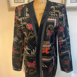 May include: Black velvet blazer with a floral and geometric pattern in shades of red, pink, and gold. The blazer has a black velvet collar and trim. The garment is displayed on a mannequin.