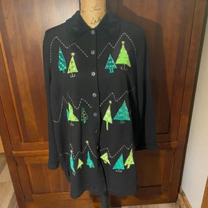 May include: Black button-down shirt with embroidered Christmas tree designs in shades of green and white stitching. The trees are adorned with gold star accents. The shirt has a black velvet collar.