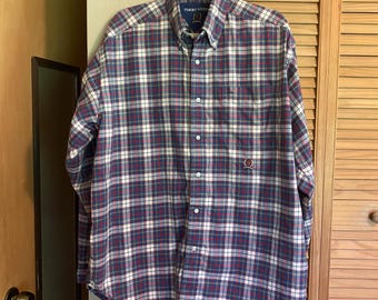May include: A long-sleeved button-down shirt in a plaid pattern of navy blue, red, white, and green. The shirt has a button-down collar, a chest pocket, and the Tommy Hilfiger logo embroidered on the chest.