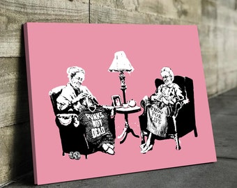 May include: Two women sit in armchairs, one wearing a sweater with the text "PUNKS NOT DEAD" and the other wearing a sweater with the text "THUG FOR LIFE". They are both knitting and sitting in front of a pink background.