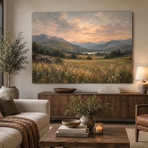 May include: A large rectangular landscape painting depicting a mountain range at sunset, featuring a grassy meadow with wildflowers in the foreground, rolling hills, and a soft, warm sky with clouds hanging over a distant lake and valley.