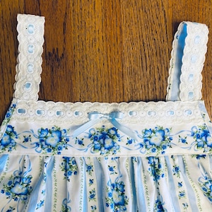 Może przedstawiać: Nocna koszula w niebiesko-biały kwiatowy wz&oacute;r z jasnoniebieską kokardą. Koszula nocna ma kwiatowy wz&oacute;r z niebieskimi kwiatami i wstążkami. Paski i dekolt są obszyte białą koronką.