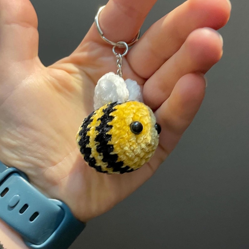 Peut inclure: Un porte-cl&eacute;s fait &agrave; la main en forme d'abeille, avec un corps ray&eacute; jaune et noir, des ailes blanches et des yeux noirs. L'abeille est attach&eacute;e &agrave; un porte-cl&eacute;s argent&eacute;. Un accessoire mignon et fantaisiste.