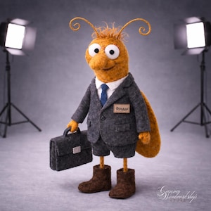 May include: A whimsical felted insect figure, dressed in a gray suit, shorts, and brown boots, holding a briefcase. The figure has large eyes, antennae, and a name tag that reads "Фредди". The background is a studio setting with lighting equipment.
