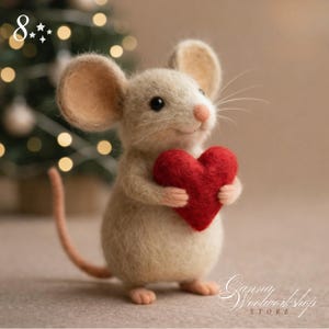 May include: A handcrafted felt mouse figurine holding a red heart. The mouse has beige fur, large ears, and a long tail. The background is blurred, with a Christmas tree visible. The figurine is from Gianna Woolworkshop Store.