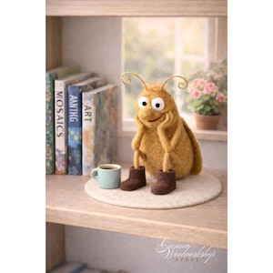 Puede incluir: Una caprichosa figura de insecto de fieltro hecha a mano con botas marrones, sentada sobre una alfombra de fieltro. Una pequeña taza azul con café está cerca. Libros y una ventana con una maceta están en el fondo.