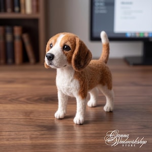 Peut inclure: Une figurine de beagle en laine feutrée avec un poitrail, un museau et des pattes blancs, ainsi que des taches brunes sur les oreilles, le dos et la queue. Le chien est debout, nez noir et yeux sombres. Le texte Ganna Woolworkshop Store est visible.