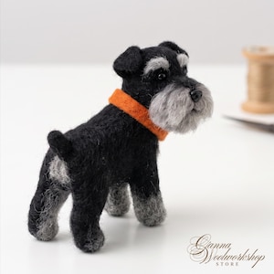 Könnte beinhalten: Eine nadelgefilzte Hunde-Figur in Schwarz und Grau mit einer strukturierten Wolloberfläche. Der Hund hat eine markante graue Schnauze, schwarze Ohren und ein leuchtend orangefarbenes Halsband. Die kleine Skulptur steht auf vier Beinen mit grauen Pfoten.