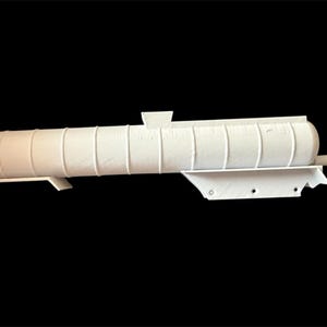 Puede incluir: Objeto cilíndrico blanco con líneas verticales y extremos redondeados, montado sobre una base blanca. Presenta una pequeña protuberancia rectangular y una extensión cilíndrica. Fondo negro. Medidas en cm.