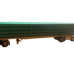May include: A semi-truck trailer loaded with a stack of green, cylindrical objects. The objects are secured and appear to be made of a durable material. The trailer is yellow and has multiple wheels.