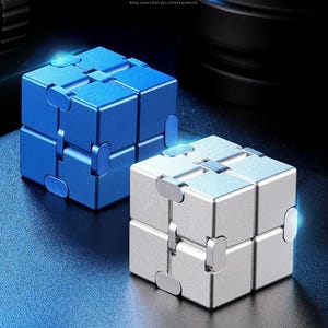 May include: Two metal fidget cubes, one blue and one silver, sit on a dark surface. The cubes are composed of smaller, connected blocks that can be manipulated. Text in the image reads: "Infinite Rubik's cube, farewell to boredom, relax. Release pressure and entertainment, Alloy cube helps you relieve pressure."
