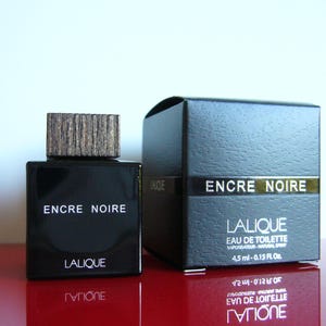 Peut inclure: Un flacon de parfum noir rectangulaire avec un bouchon en bois et une bo&icirc;te assortie. Les mots "ENCRE NOIRE" et "LALIQUE" sont imprim&eacute;s sur le flacon et la bo&icirc;te. La bo&icirc;te indique &eacute;galement un volume de 4,5 ml.
