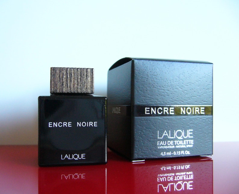 Peut inclure: Un flacon de parfum noir rectangulaire avec un bouchon en bois et une bo&icirc;te assortie. Les mots "ENCRE NOIRE" et "LALIQUE" sont imprim&eacute;s sur le flacon et la bo&icirc;te. La bo&icirc;te indique &eacute;galement un volume de 4,5 ml.