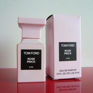 May include: A light pink Tom Ford Rose Prick Eau de Parfum bottle and box. The bottle and box have black labels with white text. The bottle contains 4 ml of perfume.