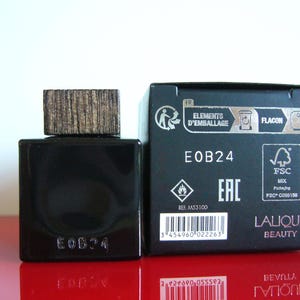 Peut inclure: Un flacon de parfum noir avec un bouchon en bois et une bo&icirc;te noire assortie. Le flacon et la bo&icirc;te portent l'inscription "EOB24". La bo&icirc;te porte &eacute;galement l'inscription "Lalique Beauty".