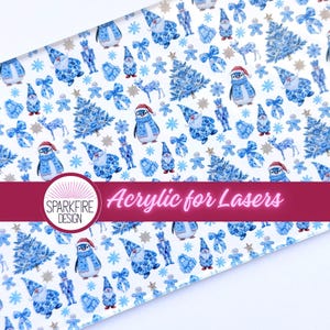 May include: A clear acrylic sheet featuring a repeating pattern of blue and white Christmas-themed illustrations including penguins, gnomes, nutcrackers, reindeer, pine trees, bows, and snowflakes. A logo reads Sparkfire Design Acrylic for Lasers.