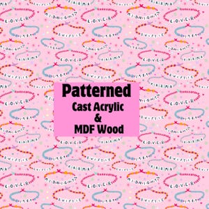 May include: Pink patterned design featuring repeating bracelets with text like "LOVE-R", "MIDNIGHTS", "KARMA", and "SWIFTIE". The design also includes stars and hearts. The text "Patterned Cast Acrylic & MDF Wood" is in a pink rectangle.