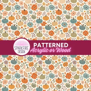 May include: A repeating pattern featuring orange, blue, and cream pumpkins interspersed with orange, blue, and cream flowers and green leaves. A dark pink horizontal banner across the centre displays the text SPARKFIRE DESIGN PATTERNED Acrylic or Wood.