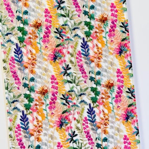 May include: A vibrant floral pattern featuring a variety of colorful wildflowers and foliage. The design includes pink, yellow, blue, green, and orange hues, creating a lively and detailed botanical print on a white background.