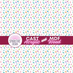 May include: A white background is covered with a pattern of colorful sprinkles in various colors, including pink, blue, green, and orange. A dark red banner with the text "CAST Acrylic and MDF Wood" is at the bottom. The Sparkfire Design logo is in a circle.