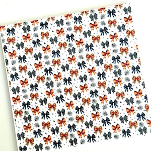 May include: White patterned fabric featuring a repeating design of orange and navy blue bows, spiderwebs, and crescent moons. The bows have a watercolor effect. This fabric is suitable for crafting and seasonal projects.