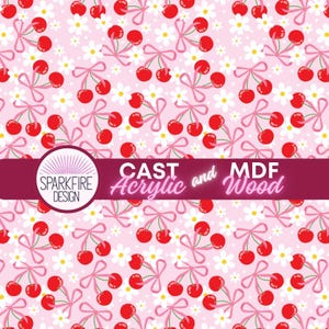 May include: A pink background with a repeating pattern of red cherries tied with pink bows and white daisy flowers. The image includes the text "CAST Acrylic and MDF Wood" and the Sparkfire Design logo.