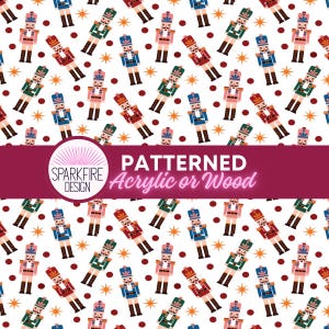 May include: A white surface featuring a repeating pattern of nutcracker figures in red, blue, and green uniforms, interspersed with dark red dots and orange starbursts. A maroon horizontal band displays the text SPARKFIRE DESIGN Patterned Acrylic or Wood.