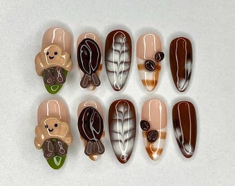 May include: A set of ten almond-shaped press-on nails with a coffee theme. Designs include coffee beans, latte art, and a smiling toast character. Colors include brown, white, beige, and green.