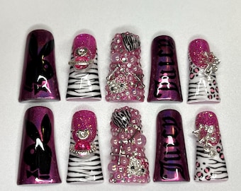 May include: A set of ten artificial nails with various designs. Some nails feature a black Playboy bunny logo on a purple background. Others have zebra stripes, rhinestones, and the word "Juicy". The nails are embellished with glitter and silver accents.