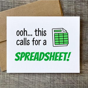 May include: A white greeting card with the text "ooh... this calls for a SPREADSHEET!" in black and green. The card features a green spreadsheet icon. The card is on a wooden surface with a brown envelope.
