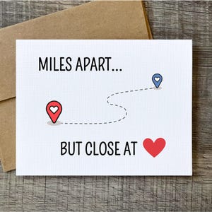 May include: A white card with the text "MILES APART... BUT CLOSE AT" and a red heart. A dotted line connects two red and blue heart-shaped location markers.
