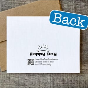 May include: Back of a white greeting card with a black and white sun graphic and the text "Happy Day" and "HappyDayCardCo.etsy.com". The text below the logo reads "Designed & printed in Idaho's beautiful Treasure Valley."