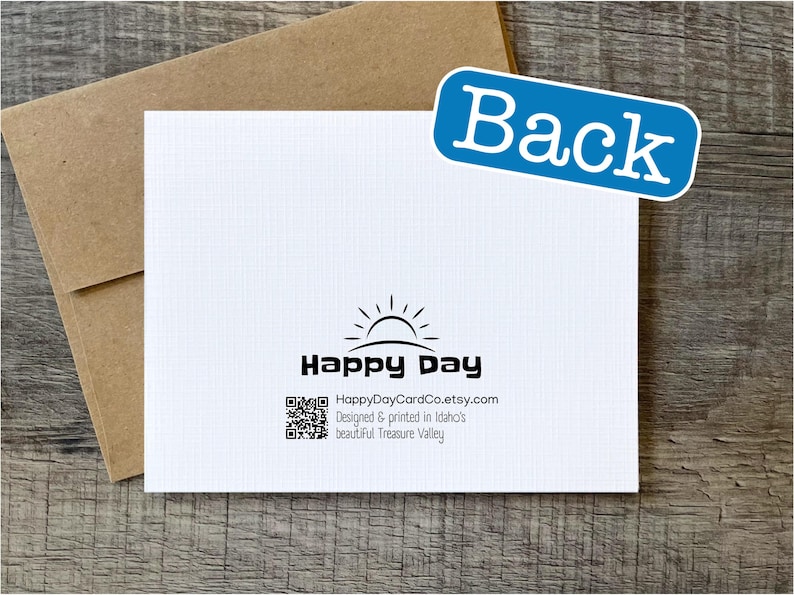 May include: Back of a white greeting card with a black and white sun graphic and the text "Happy Day" and "HappyDayCardCo.etsy.com". The text below the logo reads "Designed & printed in Idaho's beautiful Treasure Valley."