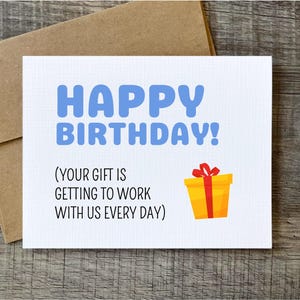 May include: A white birthday card with blue text that reads "HAPPY BIRTHDAY!". Below the text is the message "(YOUR GIFT IS GETTING TO WORK WITH US EVERY DAY)". A yellow gift box with a red ribbon is on the card.