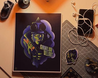 May include: A square print with a ghoulish character in a top hat and the words "Ghoulish Delight." The image is surrounded by small figurines, a sticker, and a black media player with white earbuds. The items are arranged on a gray cutting mat.