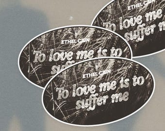 May include: Three oval-shaped stickers featuring a black and white photograph of tall grass. Each sticker displays the text ETHEL CAIN at the top and the phrase To love me is to suffer me in a white, textured, distressed font across the center.